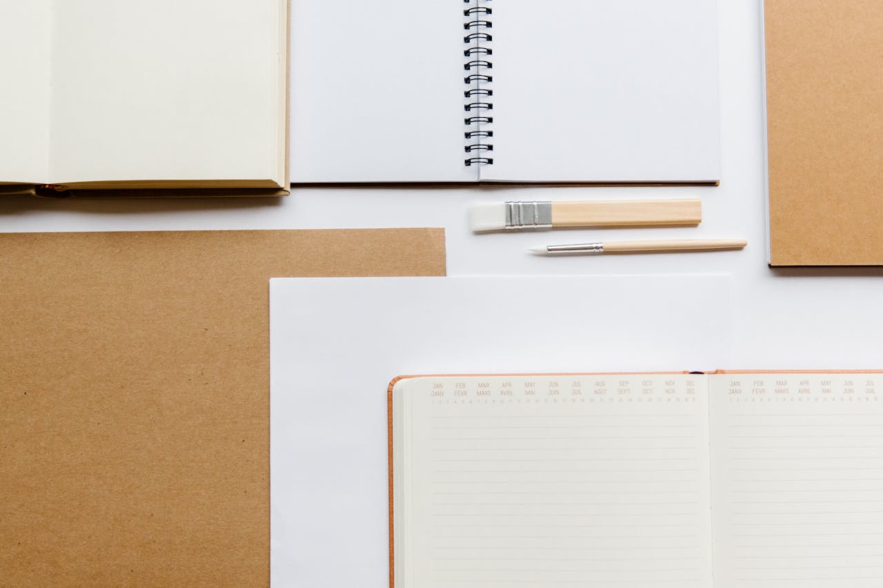 about-us Flat lay of various notebooks and stationery items on a white and brown background.